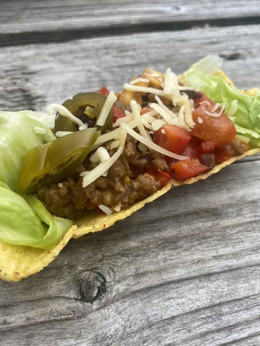 Taco met gehaktvulling, jalapeño en kaas op een houten tafel